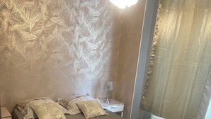 Ein Schlafzimmer mit Bett, Kissen, einem Nachttisch, einer Lampe und einem Fenster mit Vorhängen.