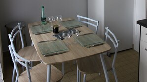 A dining area with a wooden table set for four, surrounded by white chairs. A large wall clock is mounted above the table. - Charmant Appartement Annecy Avec Vélos et Parking Classé 3 Étoiles (Annecy)