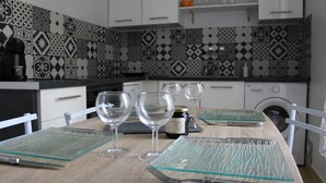 A kitchen with patterned backsplash, white cabinets, and a dining table set with wine glasses and a jar. - Charmant Appartement Annecy Avec Vélos et Parking Classé 3 Étoiles (Annecy)