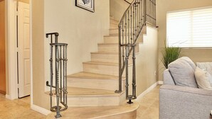 A staircase with a metal railing, a framed picture on the wall, and a grey couch in the foreground. - Beauty by the Beach Socal Fun! (Long Beach)