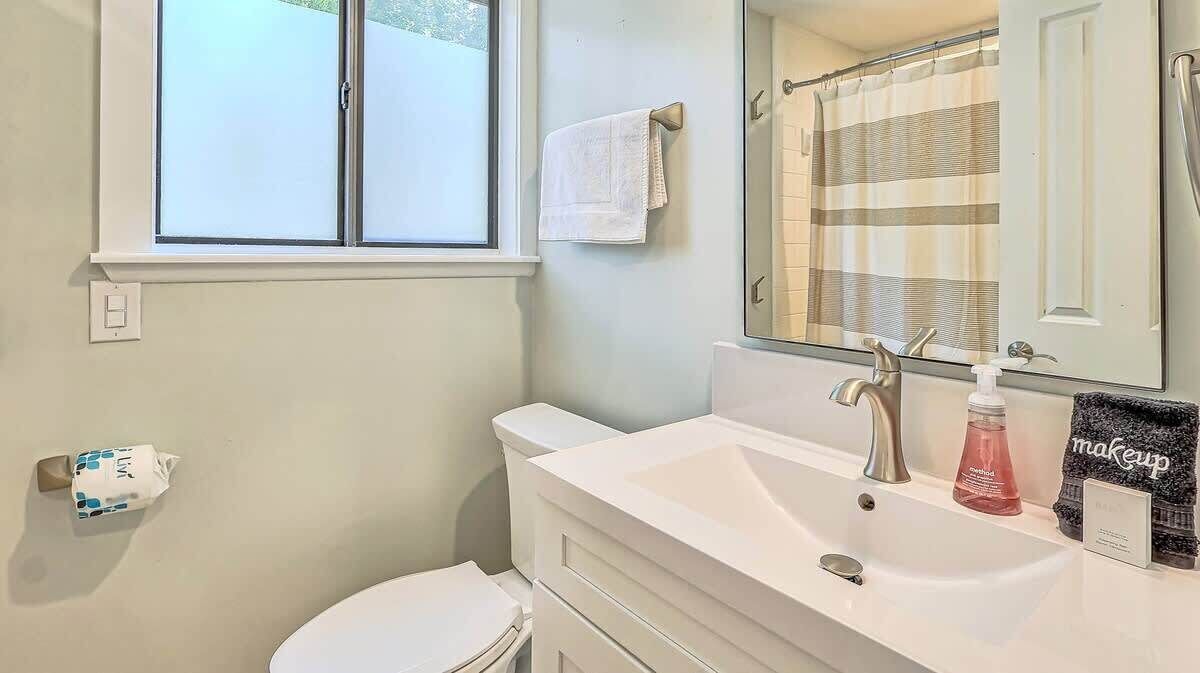 Un baño con ventana, lavamanos blanco, espejo, toalla y retrete.