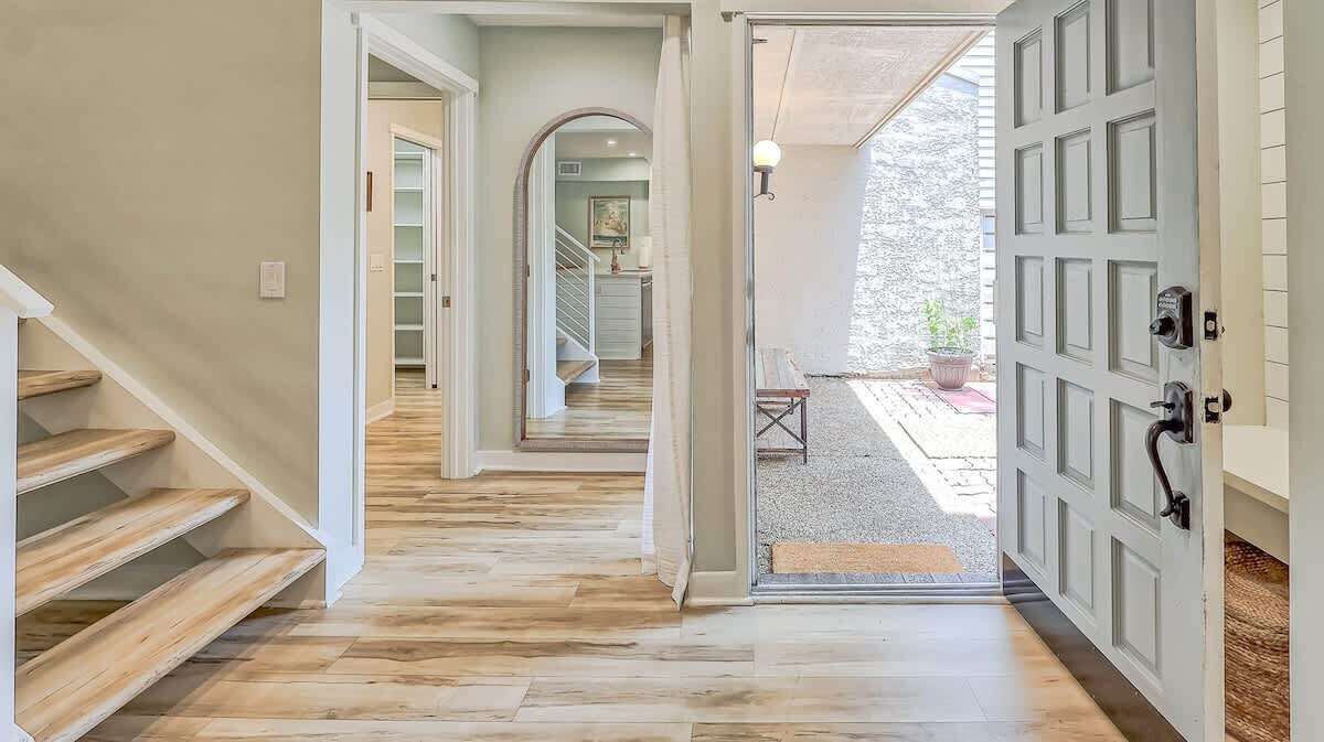 Un corridoio con pavimento in legno, una scala e una porta che dà su uno spazio esterno.