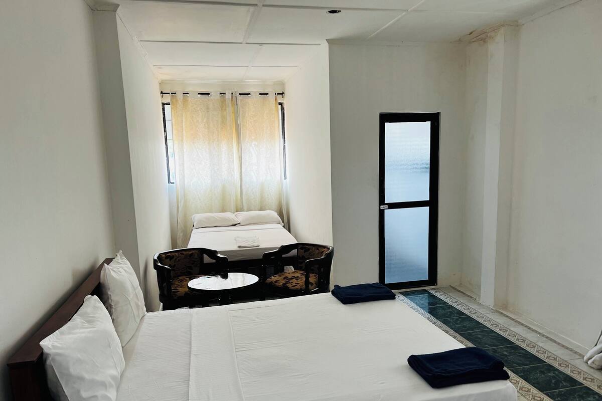 Hotellihuone, jossa on sänky, tuoli, pieni pöytä ja ikkuna, jossa on verhot.