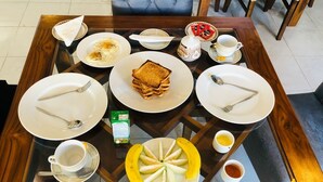 A breakfast setting with plates of eggs, toast, and fruit on a glass-top table. - Ramlyn Guesthouse Negombo (Negombo)