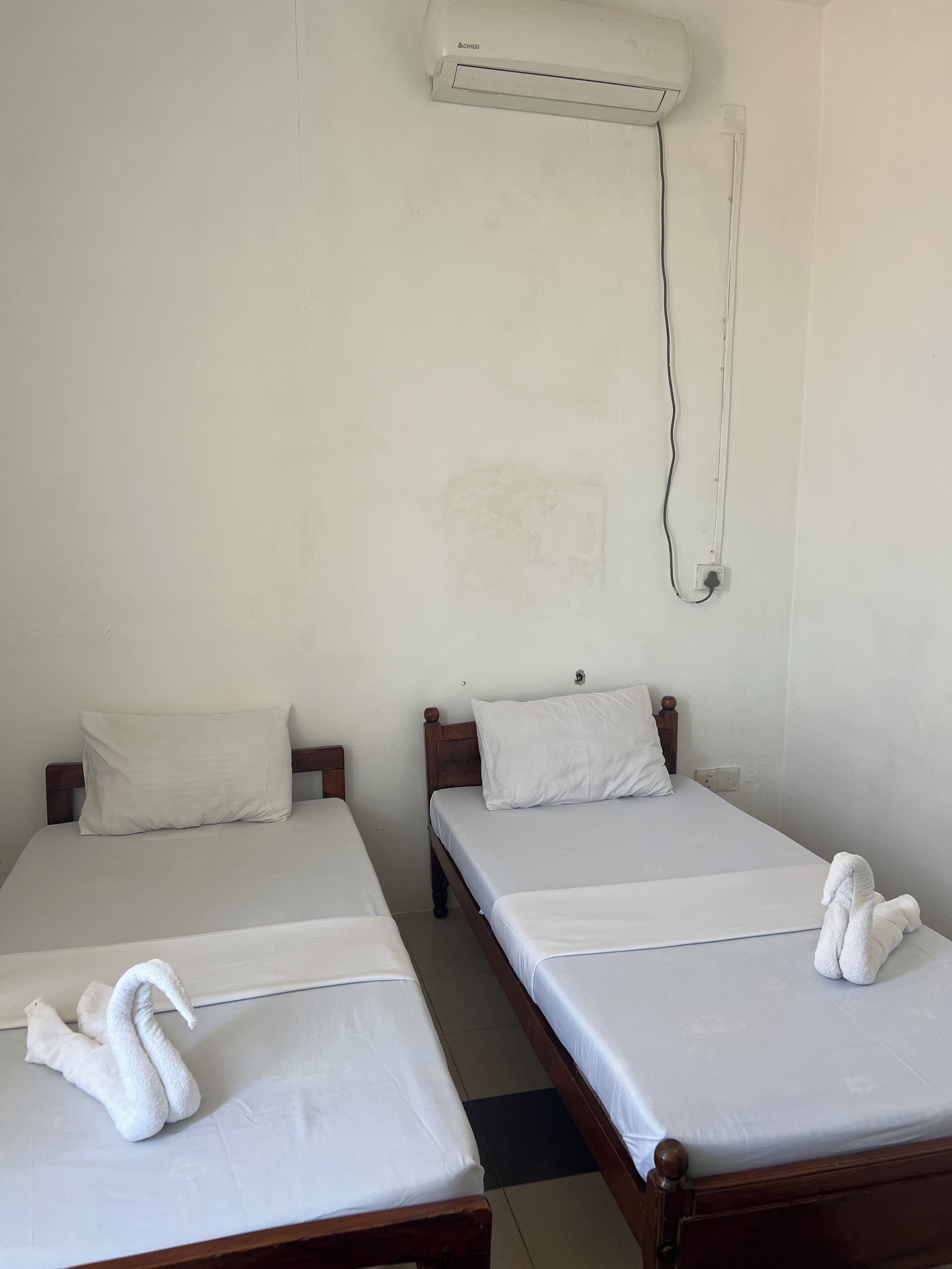 Two single beds with white linens and pillows, a wooden headboard, and an air conditioning unit mounted on the wall.