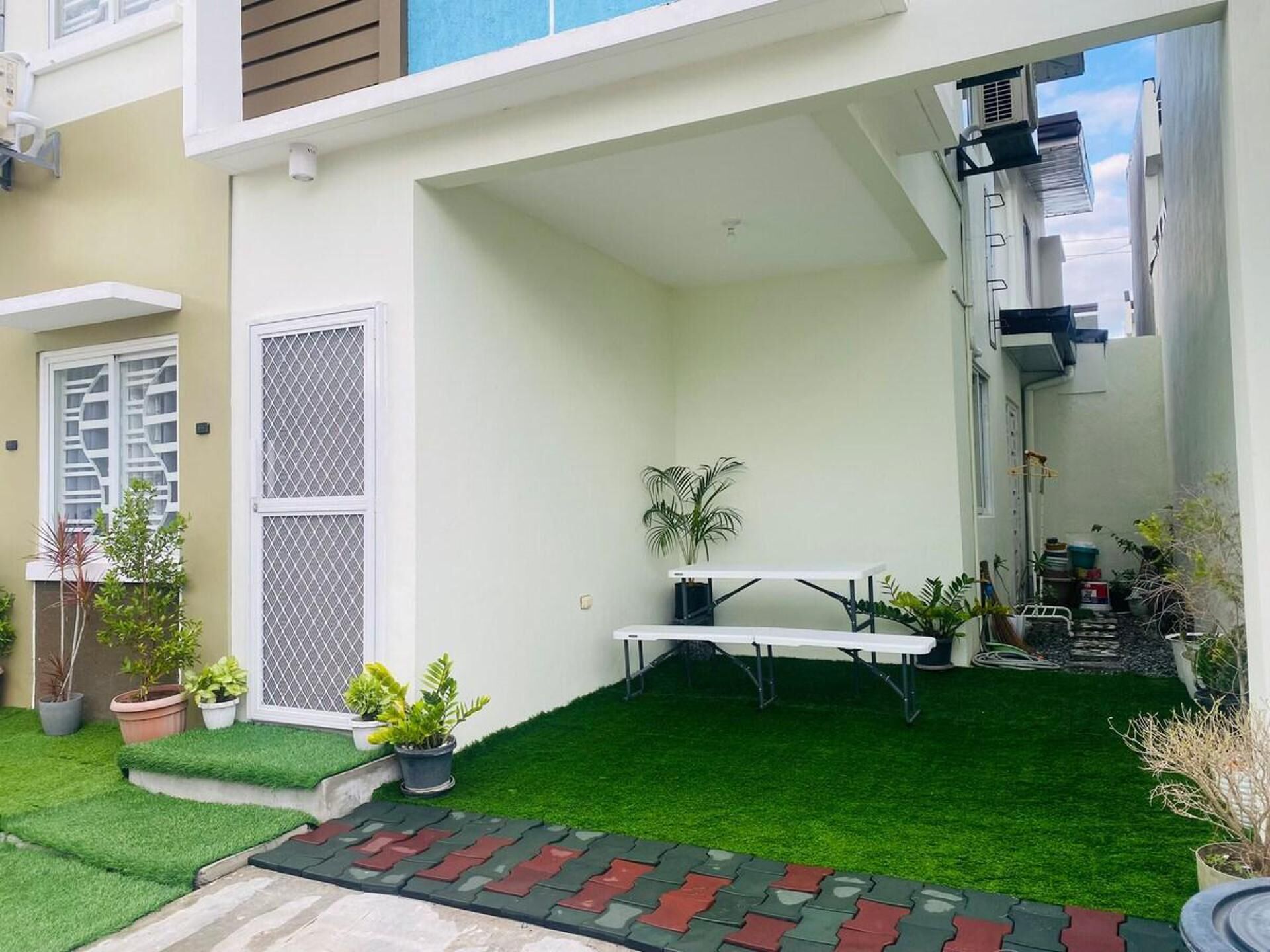 A small, enclosed outdoor space with artificial grass, a white table, and potted plants.