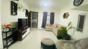 Een woonkamer met een televisie, bank, voetenbankje en een klok aan de muur.