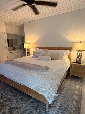 Un dormitorio con una cama, dos mesitas de noche, un ventilador de techo y un espejo.