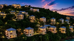 Una zona residencial costera con varias casas de dos pisos, algunas con balcones, rodeada de exuberante vegetación y con vistas a un mar azul y transparente.