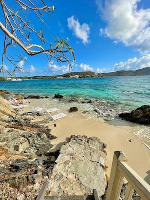 Ein Strand mit klarem türkisblauem Wasser, felsigem Ufer und einem Boot in der Ferne.