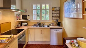 A compact kitchen with a stove, microwave, sink, and dishwasher. There is a window with a view of greenery outside.