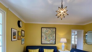 A living room with two blue sofas, a white coffee table, a star-shaped hanging light, a map on the wall, and a clock.