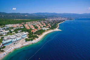 An aerial view of a coastal town with a beach, residential buildings, and a clear blue sea.