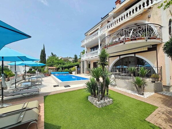 A pool area with lounge chairs, a small pool, and a well-maintained lawn.