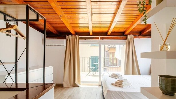 A bedroom with a wooden ceiling, a bed with white linens, a wooden desk, and a view of the outside through a glass door. - La Terrazza su Brescia · Panoramic terrace (Brescia)