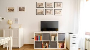 A modern living room with a flat-screen TV, a white cabinet with books, and framed pictures on the wall. - La Terrazza su Brescia · Panoramic terrace (Brescia)