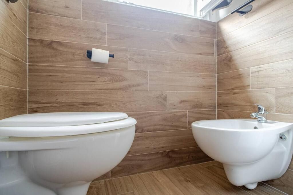 Ein Badezimmer mit Toilette und Bidet, Holzwandfliesen sowie einem sichtbaren Toilettenpapierhalter.