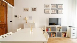 A modern living room with a white dining table, chairs, a TV, and a bookshelf. - La Terrazza su Brescia · Panoramic terrace (Brescia)