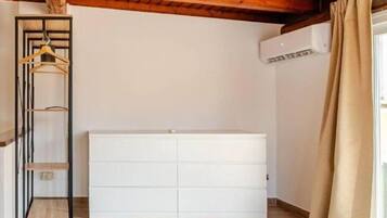 A bedroom with a wooden ceiling, a white dresser, a bed with white linens, and a wooden shelf unit.