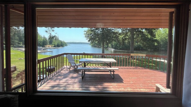 Een terras met tafel en stoelen met uitzicht op een meer, omringd door bomen en een houten balustrade.