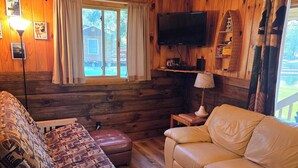 Een gezellig houten kamer in chaletstijl, met een bank, een divan, een televisie en een raam met gordijnen.