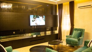 Un salon moderne avec un téléviseur à écran plat fixé à un mur foncé, un canapé, deux fauteuils et une table basse.