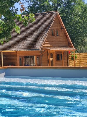 Une cabane en bois avec un toit en tuiles, une piscine et une terrasse en bois.