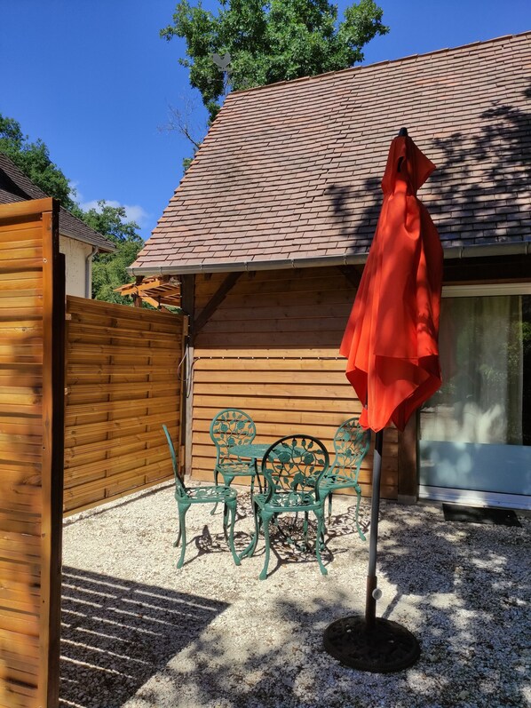 Une maison en bois avec un toit en tuiles, une terrasse en gravier et une table et des chaises en métal vert.
