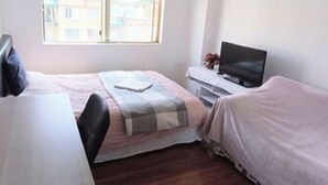 A bedroom with a bed, a TV, a window, and a desk.