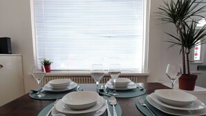 Ein Esstisch mit Tellern, Schüsseln und Besteck, nahe einem Fenster mit Jalousien.