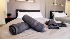 Ein ordentlich bezogenes Bett mit aufgerollten Handtüchern und einem kleinen Topf mit Pflanze auf einem Nachttisch.