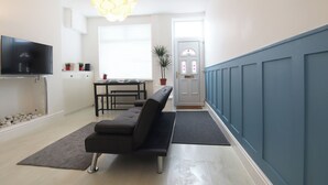 Ein modernes Wohnzimmer mit Flachbildfernseher, einer Couch, einem Esstisch und einer Topfpflanze.