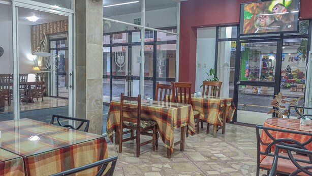 Interno di un ristorante con tavoli ricoperti da tovaglie a quadri, sedie di legno e una parete divisoria in vetro che separa la sala da pranzo dalla strada.
