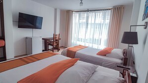 Camera d'albergo con due letti, televisione, scrivania e finestra con tende.