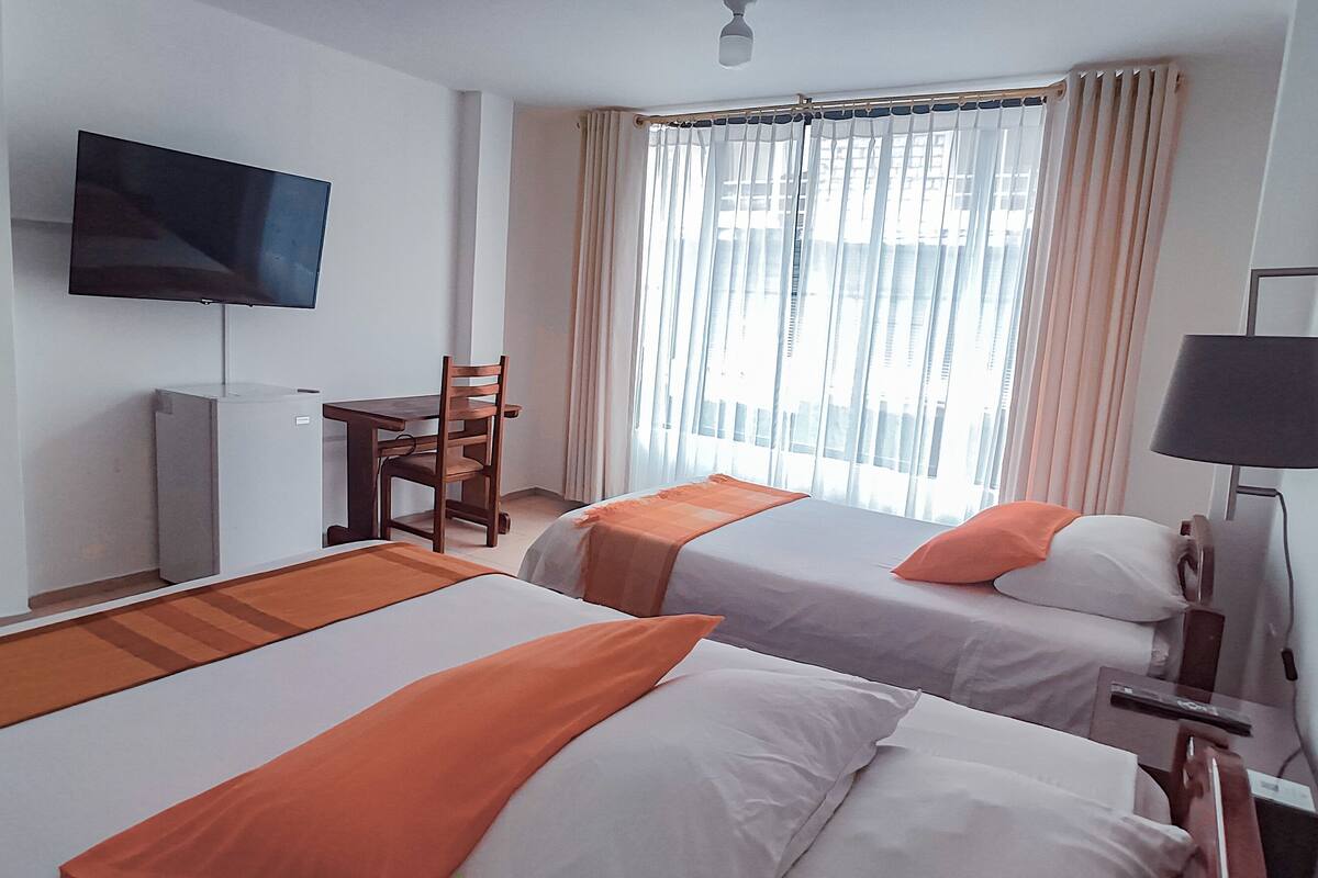 Habitación de hotel con dos camas, televisión, escritorio y ventana con cortinas.