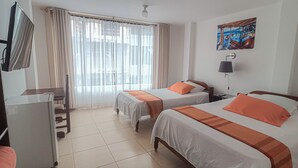 Una camera d'albergo con due letti, una scrivania, una televisione e una finestra con tende.
