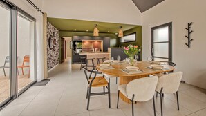 A modern dining area with a round wooden table, six chairs, and a vase of flowers. - Maison Simone - Belle Maison pour 6 (Lesneven)