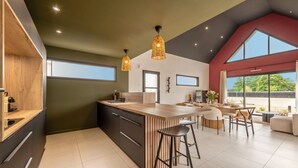 A modern kitchen with a central island, bar stools, and a dining area with a large window. - Maison Simone - Belle Maison pour 6 (Lesneven)