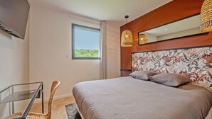 A modern bedroom with a large bed, a glass table, a wicker chair, and a large window. - Maison Simone - Belle Maison pour 6 (Lesneven)