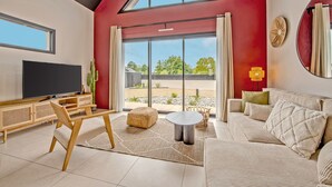 A modern living room with a large TV, a sofa, a coffee table, and a dining area with a table and chairs. - Maison Simone - Belle Maison pour 6 (Lesneven)