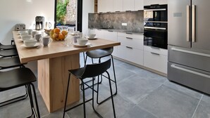 Eine moderne Küche mit einer zentralen Kochinsel, Barhocker, einer Kaffeemaschine und einem Kühlschrank.