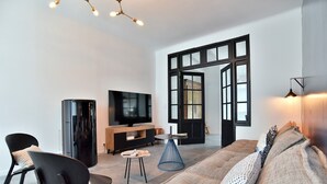 Ein modernes Wohnzimmer mit einer Couch, Sesseln, einem Fernseher und einem Esstisch.