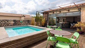 A poolside area with a wooden deck, green chairs, and a glass-enclosed patio. - Le Couvent des Ursulines - Appt climatisé, piscine (Narbonne)