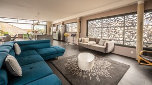 A spacious living area with a blue sectional sofa, a white coffee table, and a large window with decorative lattice. - Le Couvent des Ursulines - Appt climatisé, piscine (Narbonne)