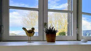 Ein Zimmer mit großen Fenstern, einer kleinen Vogel-Figur und einem Topfpflanzen.