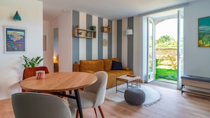 Ein modernes Wohnzimmer mit einem Holzesstisch, einer Couch und einer Bank. An der Wand befinden sich Regale mit Pflanzen und Dekoration.