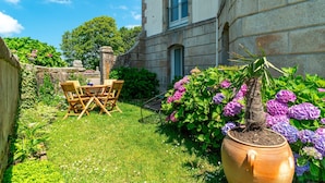 Ein Garten mit einem Holztisch und Stühlen, einem Blumentopf und violetten Blumen.