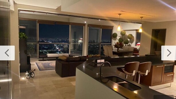 Cozinha moderna com uma ilha grande, área de refeições com cadeiras e vista da cidade à noite.