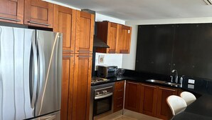 Cozinha moderna com armários de madeira, geladeira de aço inoxidável, forno e bancada preta.