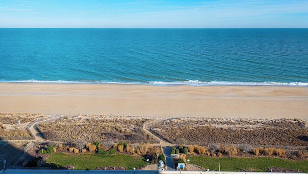 Un paysage côtier avec une plage et des dunes, offrant une vue dégagée sur l’océan et un sentier menant à une construction.